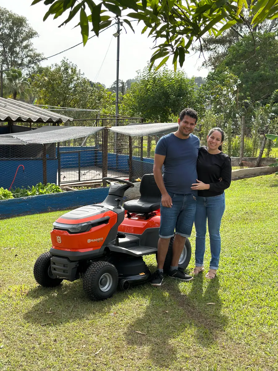 Casal de clientes com o trator cortador Husqvarna no quintal de casa