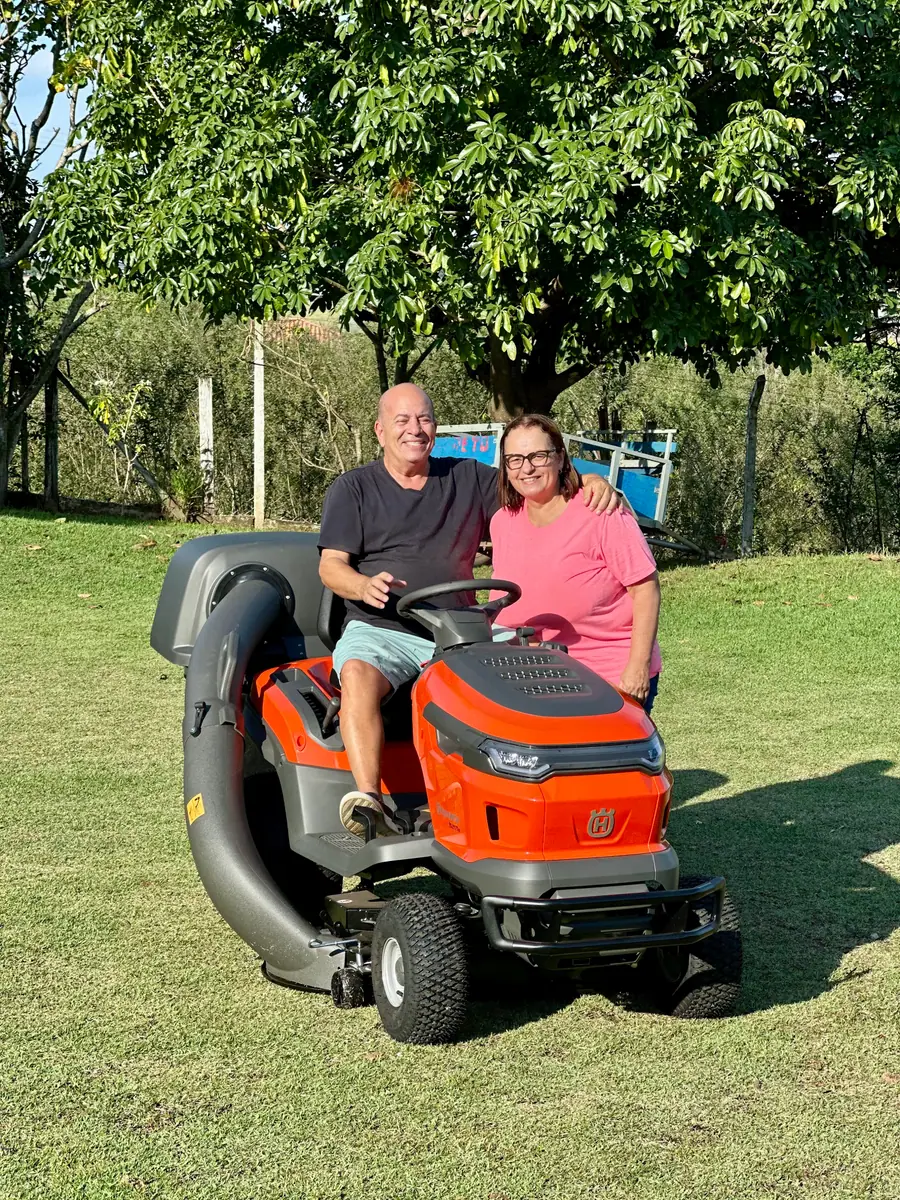 Casal de clientes com o trator cortador Husqvarna com coletor de grama, na propriedade