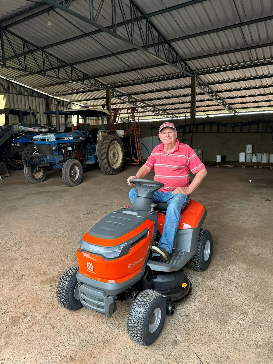 Cliente no seu novo trator cortador Husqvarna, no galpão do sítio
