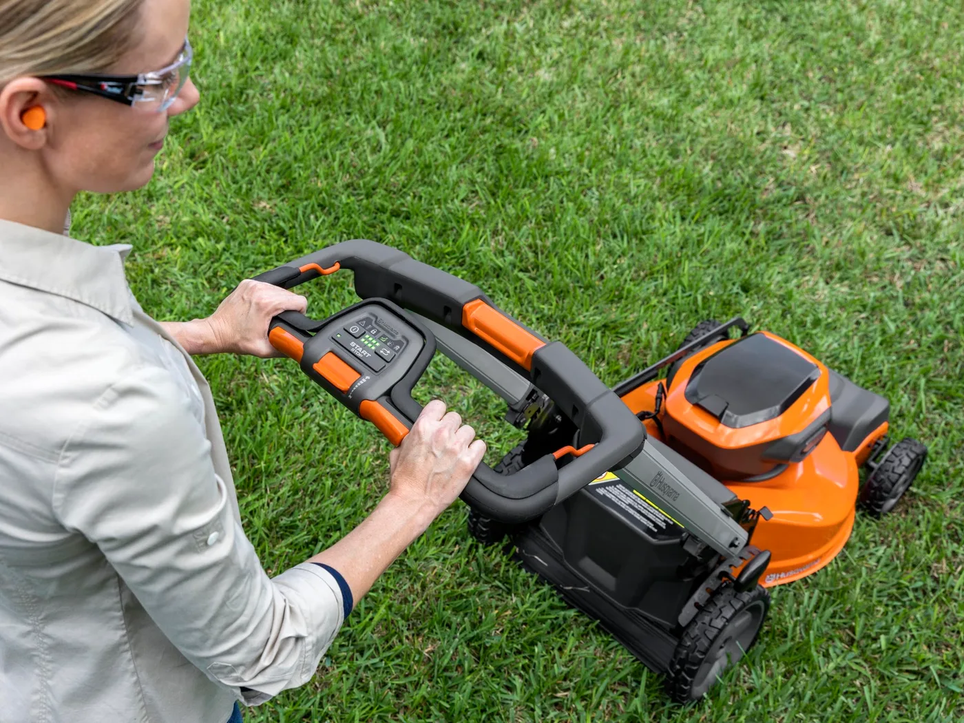 Mulher dando partida em um cortador de grama a bateria Husqvarna no gramado