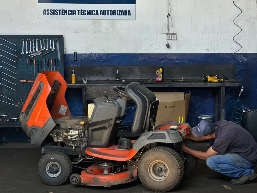 Técnico da Vardão em manutenção de um trator cortador Husqvarna, com a placa de Assistência Técnica Autorizada Husqvarna ao fundo